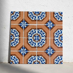 Könnte beinhalten: Ein Quadrat aus Keramikfliesen mit einem sich wiederholenden Muster. Die Fliesen haben eine warme orangebraune Farbe mit einem geometrischen Design in Blau und Braun. Das Design zeigt stilisierte florale Elemente und achteckige Formen.
