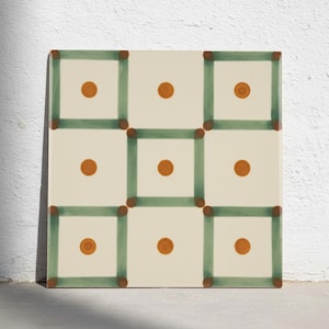 Puede incluir: Un azulejo de cerámica cuadrado con fondo color crema y una cuadrícula de líneas verdes pintadas a mano que forman nueve cuadrados distintos. Cada cuadrado contiene un punto circular sólido de color naranja-marrón centrado.