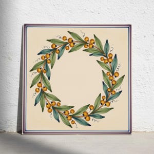 May include: A square ceramic tile featuring a hand-painted wreath design. The wreath consists of green leaves and clusters of small yellow berries arranged in a circle against a cream background, framed by a thin purple and blue border line.
