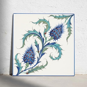 May include: A square ceramic tile with a white background and a blue border. The surface features a hand-painted botanical design of two blue thistle-like flowers with intricate scale patterns, surrounded by swirling teal and green leaves.