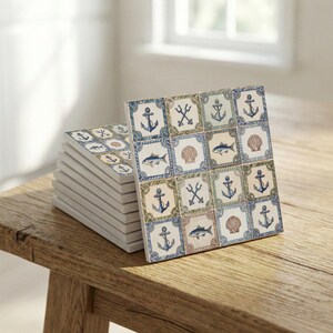 May include: A stack of square ceramic coasters with a nautical theme. Each coaster features a repeating pattern of anchors, fish, seashells, and tridents in blue, green, and tan on a white background. The coasters are displayed on a wooden surface.