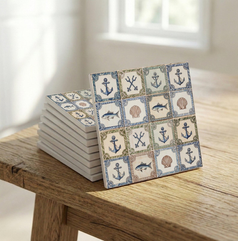 May include: A stack of square ceramic coasters with a nautical theme. Each coaster features a repeating pattern of anchors, fish, seashells, and tridents in blue, green, and tan on a white background. The coasters are displayed on a wooden surface.