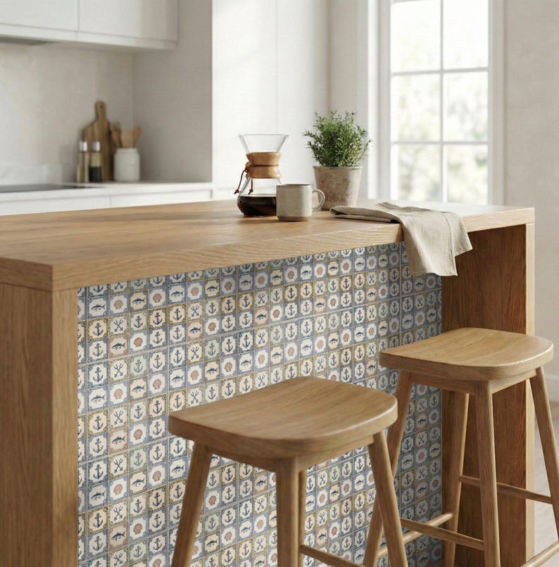 May include: A kitchen island with a wooden countertop and a decorative tile backsplash featuring nautical symbols. Two wooden stools are in front of the island. A coffee maker, mug, and potted plant are on the countertop. The color scheme is neutral with blue and brown accents.