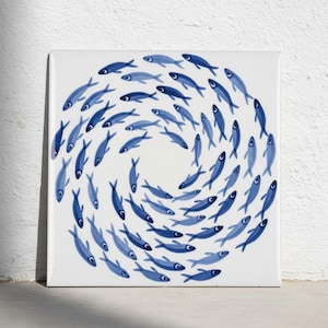 May include: A square ceramic tile featuring a circular pattern of numerous small blue fish swimming in a spiral formation against a solid white background. The fish are depicted in varying shades of blue, arranged to create a swirling vortex effect.