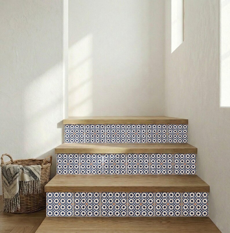 Op de afbeelding: Houten trap met decoratieve tegelstootborden. De tegels hebben een herhalend patroon van blauwe, witte en oranje cirkels. De treden zijn van lichtgekleurd hout. Een rieten mand met een deken staat ernaast.