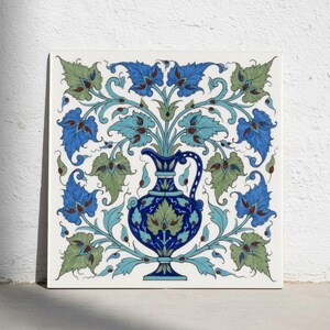 May include: A square ceramic tile featuring a central dark blue pitcher surrounded by symmetrical floral and leaf patterns in shades of light blue, green, and dark blue. The design is intricate, with swirling vines and pointed leaves.