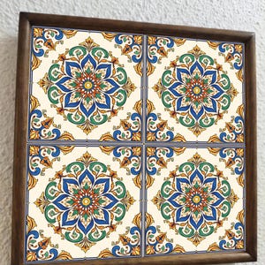 May include: A square wooden frame holds four decorative tiles. Each tile features a symmetrical floral design in blue, green, orange, and yellow against an off-white background. The tiles are framed by a dark brown wooden border.