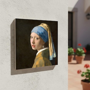 Puede incluir: Arte mural cuadrado con un retrato de una joven con un pendiente de perla. La pintura representa a una mujer con un pañuelo azul y amarillo y una chaqueta amarilla y verde sobre un fondo oscuro. La obra de arte está montada en un marco de madera.