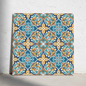 Op de afbeelding: Vierkante canvas kunst met een herhalend bloemenpatroon in blauw, geel, oranje en wit. Het ontwerp heeft een symmetrische, tegelachtige opstelling met ingewikkelde details. Het kunstwerk wordt tentoongesteld tegen een witte muur.