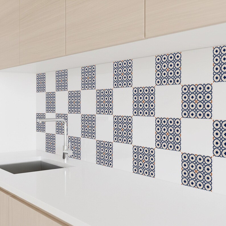 Op de afbeelding: Witte keukentegels met een herhalend geometrisch patroon in marineblauw, oranje en wit. De tegels zijn ge&iuml;nstalleerd boven een wit aanrecht en een gootsteen, met licht houten kasten erboven.