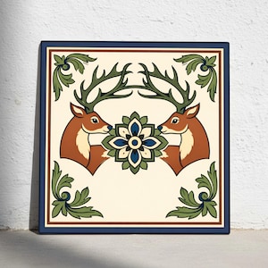 Könnte beinhalten: Quadratische dekorative Fliese mit zwei sich gegenüberstehenden Hirschen mit großem Geweih und braunem Fell. Zwischen ihnen befindet sich ein blaues, grünes und weißes Blumenmuster. Grünes und cremefarbenes Laub befindet sich in den Ecken. Die Fliese hat einen dunkelblauen Rand.