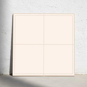 Puede incluir: Una baldosa cuadrada de color crema con un borde y líneas de cuadrícula de color beige claro, apoyada contra una pared blanca. La baldosa está dividida en cuatro secciones iguales.