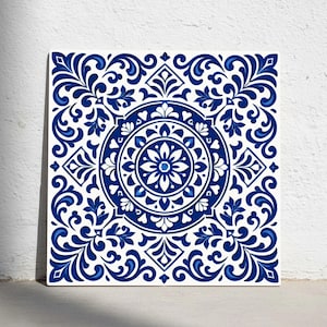 Puede incluir: Azulejo cerámico cuadrado con un detallado patrón floral azul y blanco. El diseño presenta un medallón floral central rodeado de adornos y formas geométricas. El azulejo está sobre un fondo blanco.