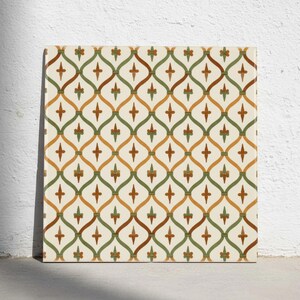 Op de afbeelding: Een vierkante keramische tegel met een herhalend ogee-patroon in saliegroen en gebrand oranje op een gebroken witte achtergrond. Het ontwerp bevat kleine, centraal geplaatste kruisvormige motieven in elk gebogen gedeelte van het raster.