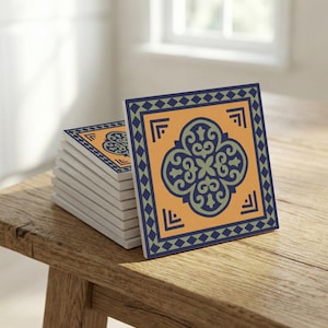 Puede incluir: Una pila de posavasos cuadrados de cerámica con un diseño geométrico repetitivo. Cada posavasos presenta un patrón floral central en azul y verde sobre un fondo naranja, enmarcado por un borde azul con diamantes y esquinas. Los posavasos están apilados sobre una superficie de madera.