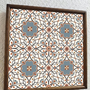 Puede incluir: Una bandeja decorativa de madera con un patrón de baldosas florales repetido. El diseño incluye motivos florales azules, naranjas y marrones sobre un fondo crema, enmarcado por un borde de madera oscura.