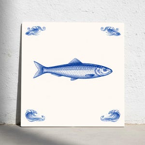 Puede incluir: Azulejo cerámico cuadrado con una ilustración azul de un pez sobre fondo crema. Motivos decorativos de olas en cada esquina. El diseño evoca el arte náutico tradicional, con una detallada representación del pez.