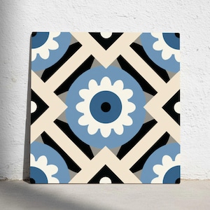 Puede incluir: Azulejo cuadrado con un patrón floral repetido en tonos azules, blancos, negros y beige. El diseño presenta flores estilizadas y formas geométricas, creando un aspecto simétrico y decorativo. El azulejo se muestra contra una pared blanca.