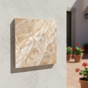 Peut inclure: Un carreau de marbre beige carré avec un motif veiné naturel. Le carreau est monté sur un mur gris clair, mettant en valeur sa surface polie et ses tons terreux. Le motif du marbre présente un mélange de beige clair et foncé avec des veines blanches.