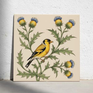 Op de afbeelding: Een vierkante keramische tegel met een handgeschilderde illustratie van een putter zittend op een groene distelplant. De vogel heeft een geel, zwart en wit verenkleed. De distelplant heeft groene bladeren en diverse ronde, gele en blauwe bloemhoofdjes.