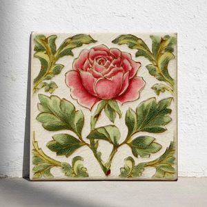 Puede incluir: Azulejo cerámico cuadrado con una ilustración detallada de una rosa rosa rodeada de hojas y vides verdes. El diseño floral se encuentra sobre un fondo crema con un efecto craquelado, creando una estética vintage. Mide aproximadamente 20 cm x 20 cm.