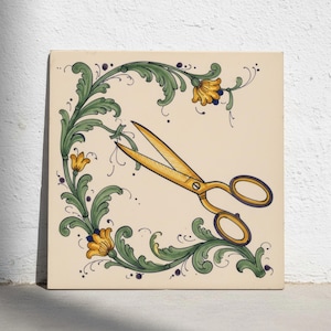 May include: A square ceramic tile with a cream-coloured background featuring a hand-painted illustration of gold-coloured scissors centred within a decorative border of green scrolling acanthus leaves and yellow flowers with dark blue accents.