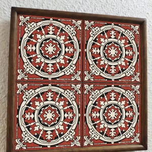 May include: A framed set of four decorative tiles. Each tile has a red background with a white and black circular design. The frame is made of dark brown wood, giving a vintage appearance.