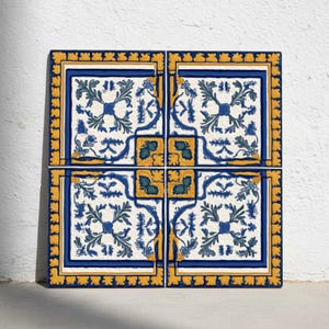 Puede incluir: Cuatro baldosas de cerámica cuadradas con un patrón floral repetitivo en azul, amarillo y blanco. Las baldosas están dispuestas juntas, formando un cuadrado más grande. El diseño presenta hojas estilizadas y formas geométricas.
