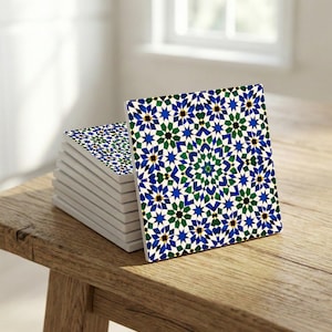 May include: A stack of square ceramic coasters with a geometric pattern in blue, green, black, and white. The coasters are displayed on a wooden surface. The coasters are approximately 10 cm square.