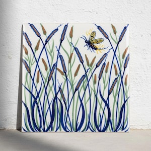 May include: A square ceramic tile with a white background featuring a hand-painted pattern of tall green and blue cattail reeds. A single yellow and black insect with wings is depicted in the upper right section, hovering above the reeds.
