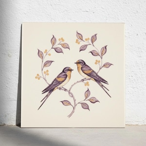 Op de afbeelding: Een vierkante muurkunstprint met twee vogels op een gebogen tak met gedempte paarse bladeren en kleine gele bessen. De vogels hebben donkergrijze vleugels, gele borstjes en lange staarten, afgebeeld tegen een effen crèmekleurige achtergrond.