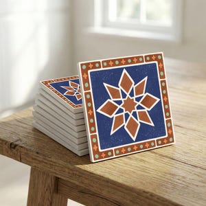 May include: A stack of square ceramic coasters with a geometric design. Each coaster features a dark blue background with a brown starburst pattern and a brown and teal border. The coasters are stacked on a wooden surface.
