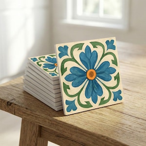 May include: A stack of square ceramic tiles with a floral design. Each tile features a blue flower with an orange center and green accents on a cream background. The tiles are stacked on a wooden surface.