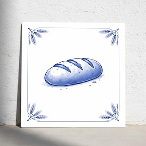 Puede incluir: Ilustración azul y blanca de una hogaza de pan sobre una baldosa cuadrada. El pan tiene tres líneas marcadas en la parte superior. La baldosa tiene un borde azul con espigas de trigo en cada esquina. El fondo es blanco.
