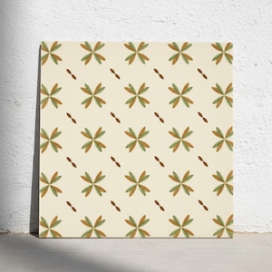 Op de afbeelding: Een vierkante tegel met een herhalend patroon van vierbladige bloemmotieven in gedempt olijfgroen en terracotta oranje op een crèmekleurige achtergrond, afgewisseld met kleine, donkerbruine diagonale streepjes tussen de bloemen.