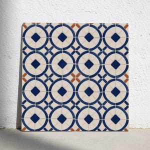 Puede incluir: Azulejo cerámico cuadrado con un patrón repetitivo de círculos, diamantes y cruces azules sobre un fondo crema. El azulejo también presenta pequeños acentos de color marrón anaranjado. El diseño es simétrico y geométrico.