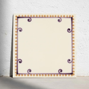 Puede incluir: Un azulejo cuadrado de cerámica con un centro color blanco hueso. El borde presenta un patrón repetitivo de pequeños puntos de color marrón claro. Dentro, una fina línea morada forma un marco rectangular con espirales en las esquinas.