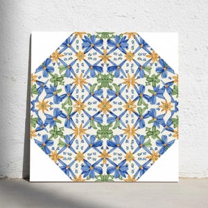 Puede incluir: Un azulejo cuadrado con un patrón octogonal y un motivo floral repetitivo. El diseño muestra flores de estilo acuarela en azul, amarillo y verde, dispuestas en una composición geométrica simétrica sobre un fondo blanco limpio.