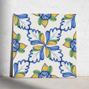 Può includere: Una piastrella in ceramica quadrata con un motivo ripetitivo di foglie stilizzate e disegni floreali in tonalità vivaci di blu, giallo e verde su sfondo bianco. Il design è composto da forme di foglie simmetriche e centri a griglia.