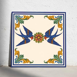 Może przedstawiać: Kwadratowa płytka ceramiczna z dwoma niebieskimi jaskółkami zwróconymi do siebie, z kwiatem pomiędzy nimi. Płytka ma kremowe tło, ciemnoniebieską obwódkę i dekoracyjne elementy narożne w kolorze żółtym, zielonym i pomarańczowym.