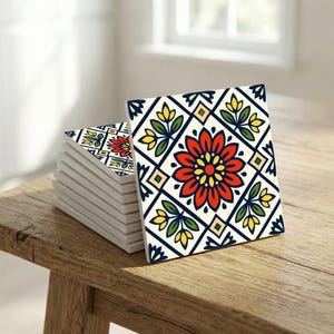 Może przedstawiać: Stos kwadratowych ceramicznych podkładek z kwiatowym wzorem. Każda podkładka ma czerwoną kwiat z żółtym środkiem, zielone liście i niebiesko-biały geometryczny wzór. Podkładki leżą na drewnianej powierzchni.