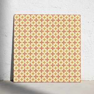 Può includere: Una piastrella quadrata con un motivo geometrico ripetitivo di rombi interconnessi. Il design è composto da motivi floreali a quattro petali rossi e dorati alternati al centro di ogni rombo, su uno sfondo color crema chiaro.