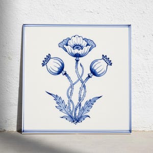 Könnte beinhalten: Eine quadratische Keramikfliese mit einer handgemalten blau-weißen Illustration einer zentralen Mohnblume in voller Blüte, flankiert von zwei geschlossenen Mohnkapseln, mit detaillierten Stängeln und Blättern, umrahmt von einer dünnen blauen Linie.