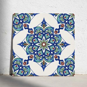 May include: A square ceramic tile featuring a symmetrical floral mandala pattern in shades of deep blue, turquoise, sage green, and dark red on a white background. The intricate design consists of repeating petal shapes and curved lines.
