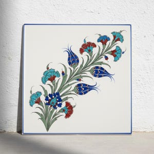 May include: A square ceramic tile with a white background and a blue border. The center features a decorative floral pattern with stylized tulips and carnations in shades of turquoise, deep blue, and red, connected by green stems and leaves.