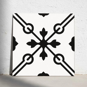 Op de afbeelding: Vierkante witte tegel met een zwart geometrisch patroon. Het ontwerp heeft een centrale kruisvorm, vier hoekaccenten en diagonale lijnen met cirkelvormige elementen. Geschikt voor vloer- of wanddecoratie.