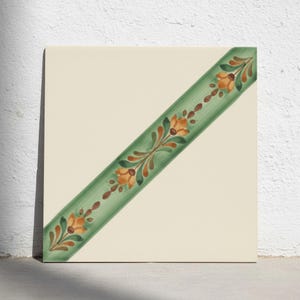 Puede incluir: Un azulejo de cerámica cuadrado con una superficie lisa de color blanco roto que presenta una banda diagonal desde la esquina superior derecha hasta la inferior izquierda. La banda es verde salvia y está decorada con un patrón repetitivo de flores naranjas y hojas verde oscuro.