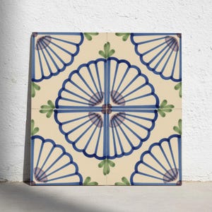 May include: A square ceramic tile featuring a cream-colored background with a repeating pattern of blue fan-shaped motifs. The design includes thin blue lines radiating from a central point, accented by small green leaf-like shapes at the corners.