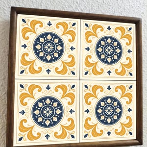 May include: A square wooden frame holds four decorative tiles. Each tile features a cream-colored background with a navy blue and yellow floral design. The design includes a central circle with a floral pattern and surrounding stylized leaves.