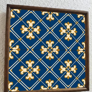 Könnte beinhalten: Quadratisches Holztablett mit dekorativem Fliesenmuster. Die Fliesen haben einen marineblauen Hintergrund mit einem sich wiederholenden Muster aus weißen diagonalen Linien, goldenen Akzenten und cremefarbenen floralen Motiven. Das Tablett hat einen dunkelbraunen Holzrahmen.